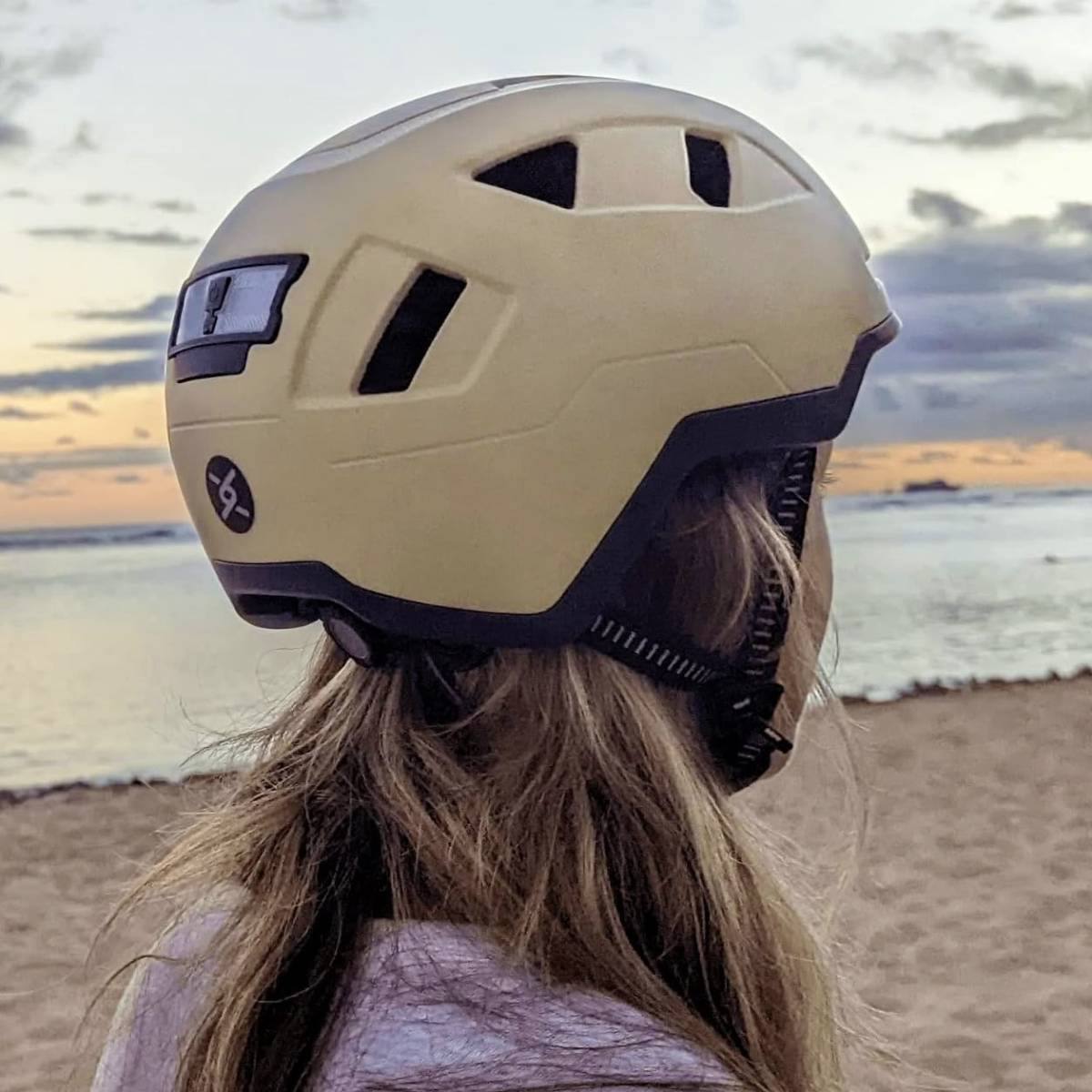 woman on the beach wearing an ebike helmet staring longingly into the sunset