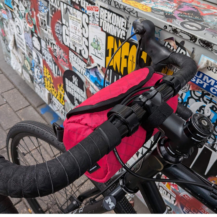 Close-up of a hot pink ecopak handlebar bag against a wall covered in stickers.