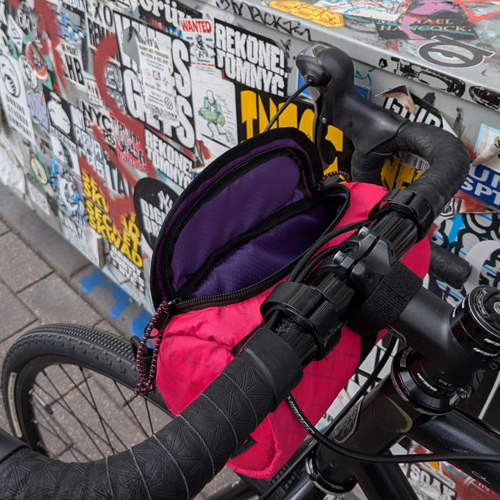 Close-up of a hot pink ecopak bike bag against a wall covered in stickers.
