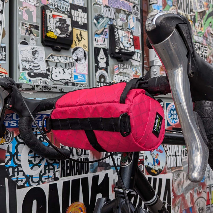 Pink bike bag on a bicycle handlebar with a colorful, sticker-covered wall in the background