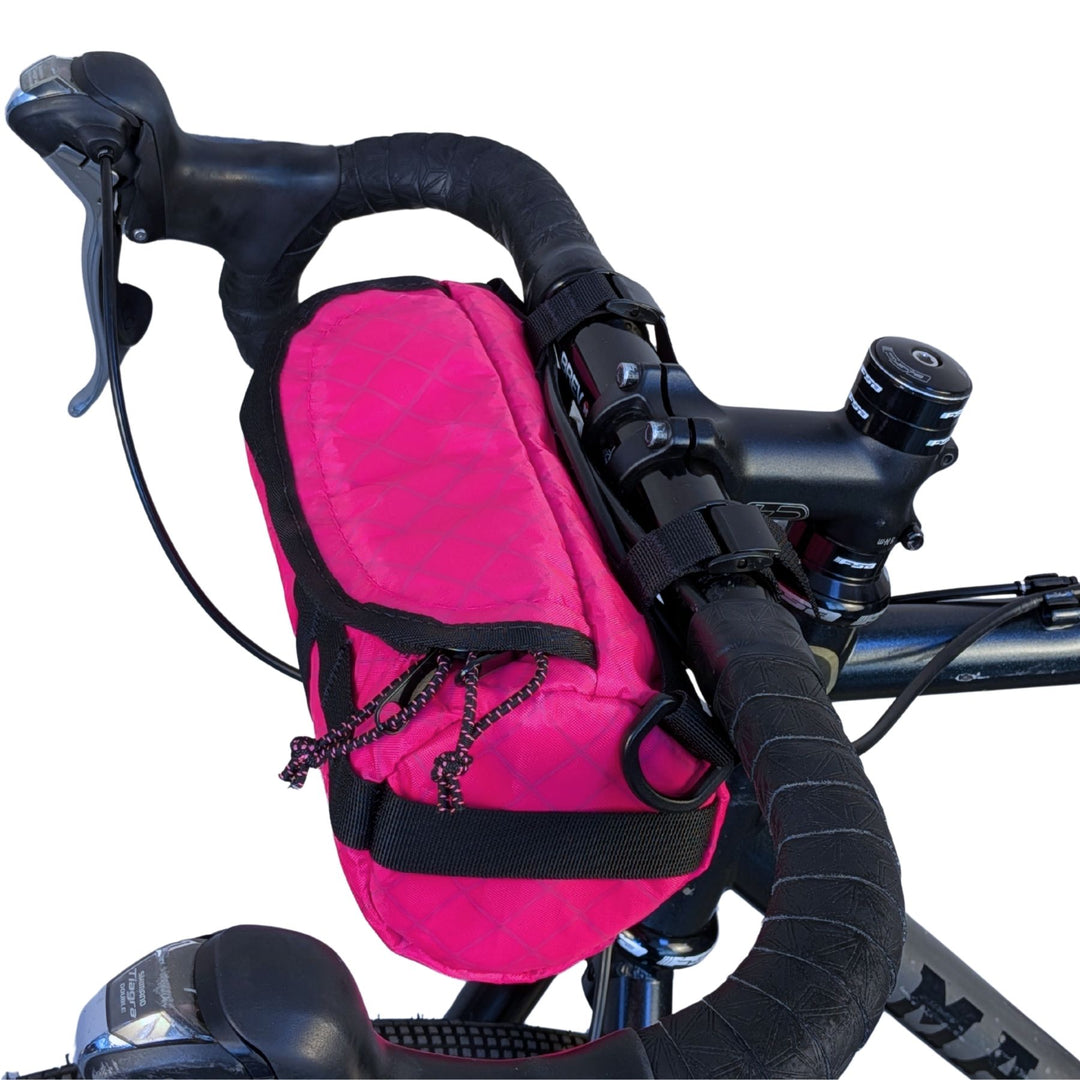 Pink ECOPAK handlebar bag attached to a gravel bike on a white background