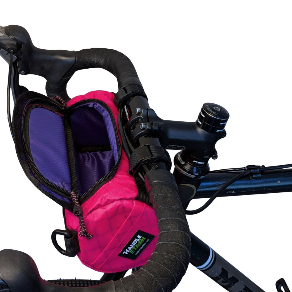 Pink ecopak and purple bike bag attached to bicycle handlebars on a white background