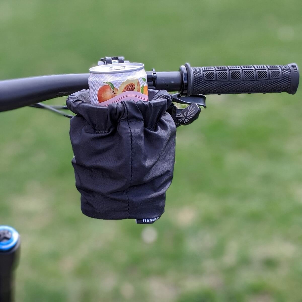 A can of peach-flavored drink is placed inside a black HandleStash cup holder attached to the handlebar of a bicycle.